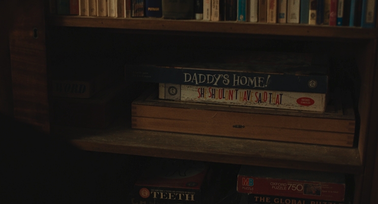 A cabinet filled with books and board games. The two games have vintage style typography: The one on top, in a blue box, is called Daddy's Home. The one below it, in a white box, is called She Shouldn't Have Said That