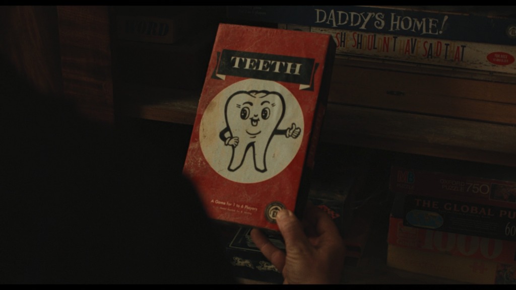 A hand holds a red game box. The name of the game is Teeth. There's a picture of an anthropomorphized smiling tooth mascot, above the text "A game for 1 to 6 players."
