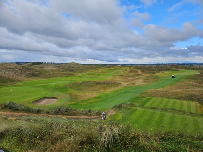 A photo from an elevated tee box of two fairways at the Island Golf Club showing rounded dunes in the rough with natural brush filling them out