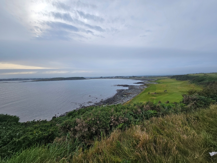 A picture of a hole from an elevated tee box of Ardglass Golf Club, the hole is right on the ocean with an island visible in the distance, as the 12th fairway runs up the entire beach and leads to a large green protected by a bunker